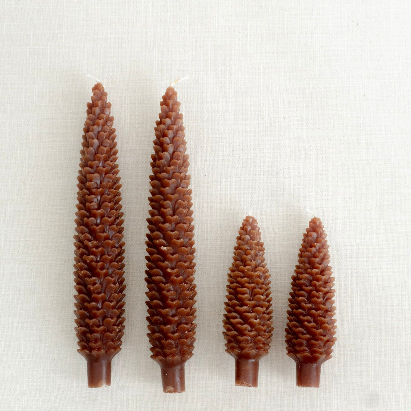 Four brown pine cone-shaped candles on a white background