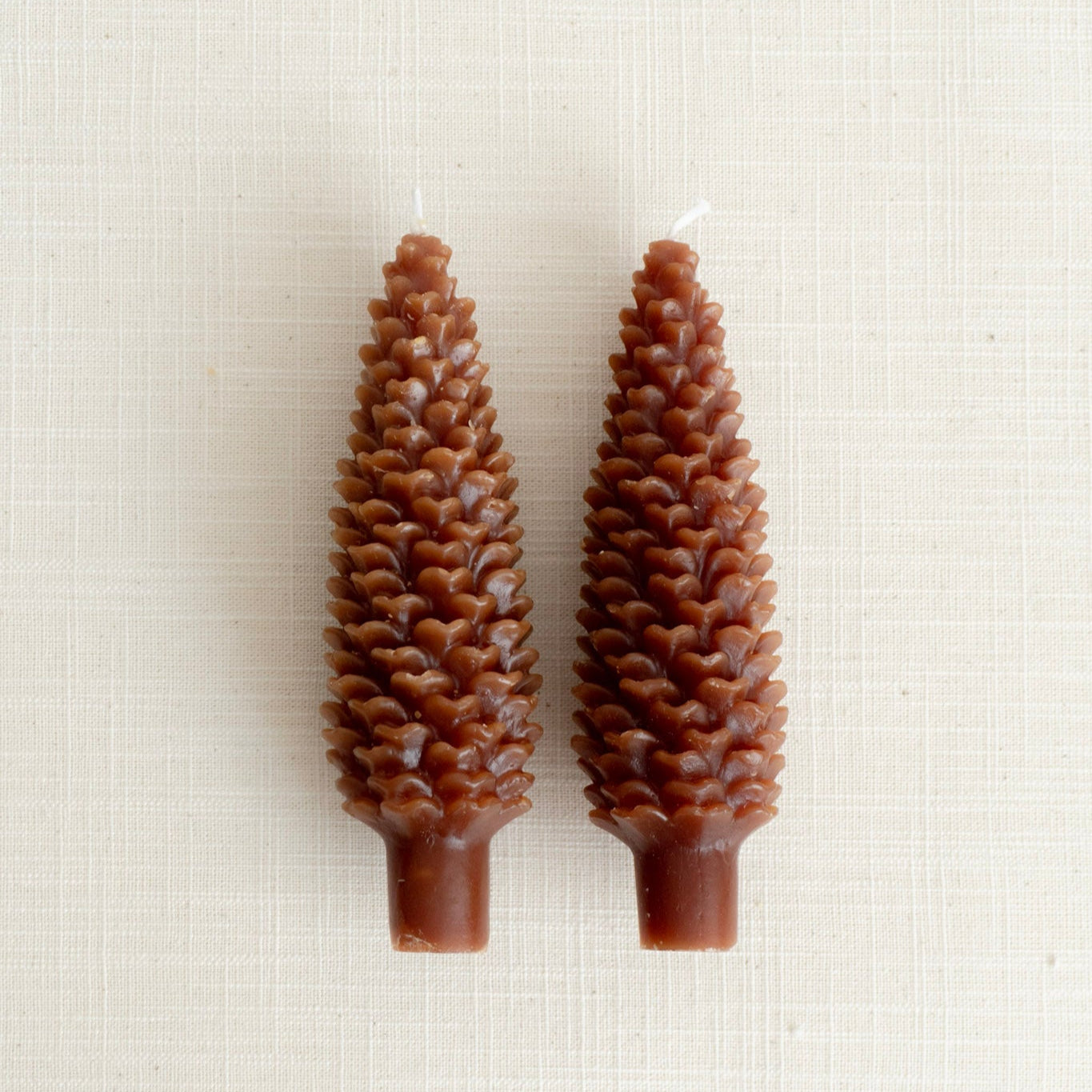 Two pine cone-shaped candles on a white background