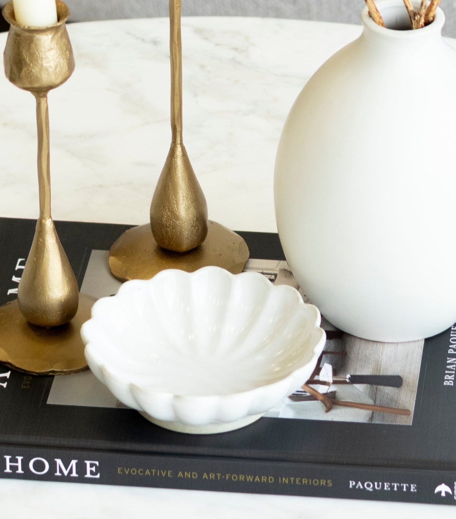 Decorative setup on a coffee table with a white vase, gold candle holders, and a book titled &