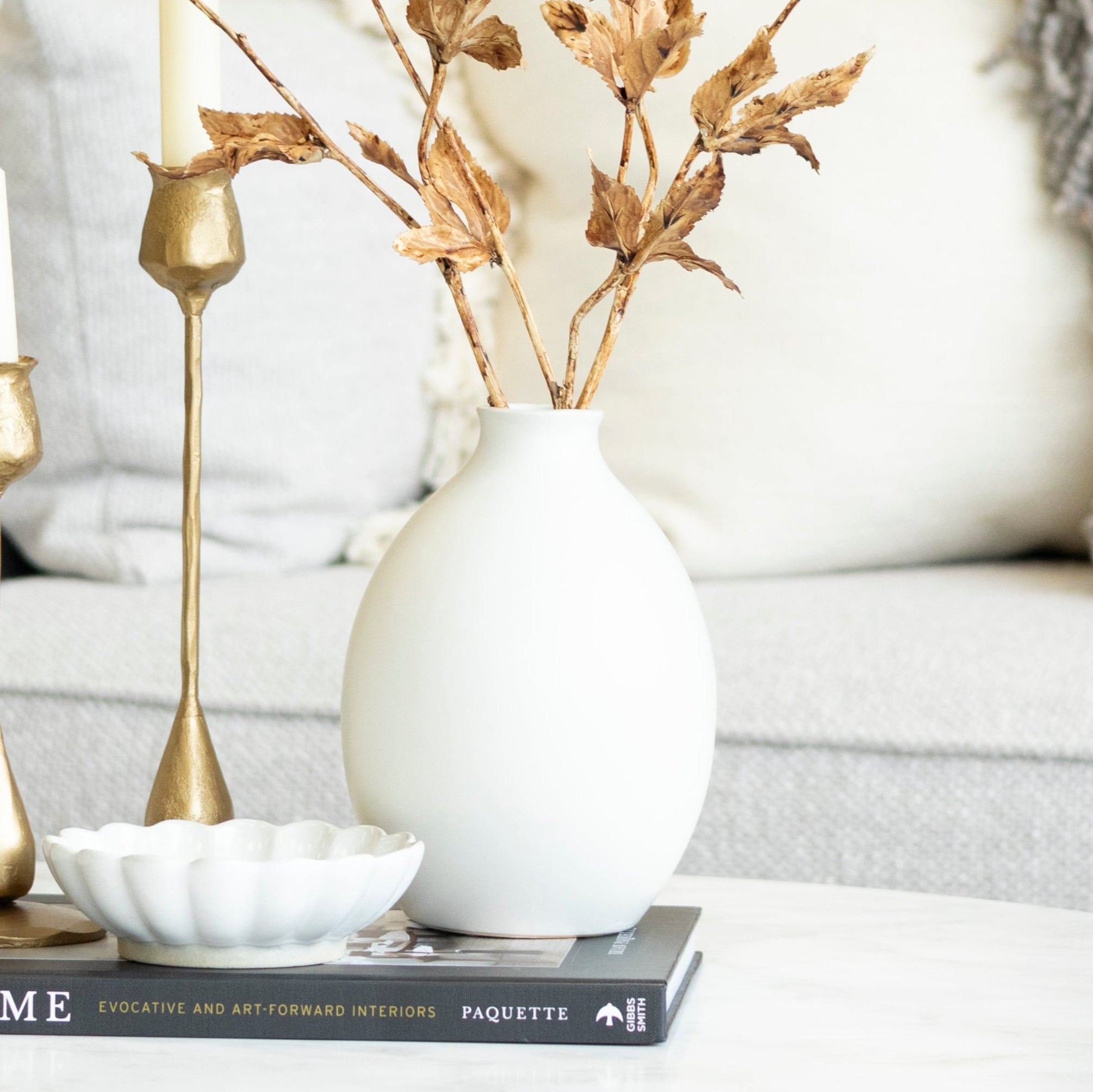 Living room with a white sofa, decorative vase, and candles on a coffee table.