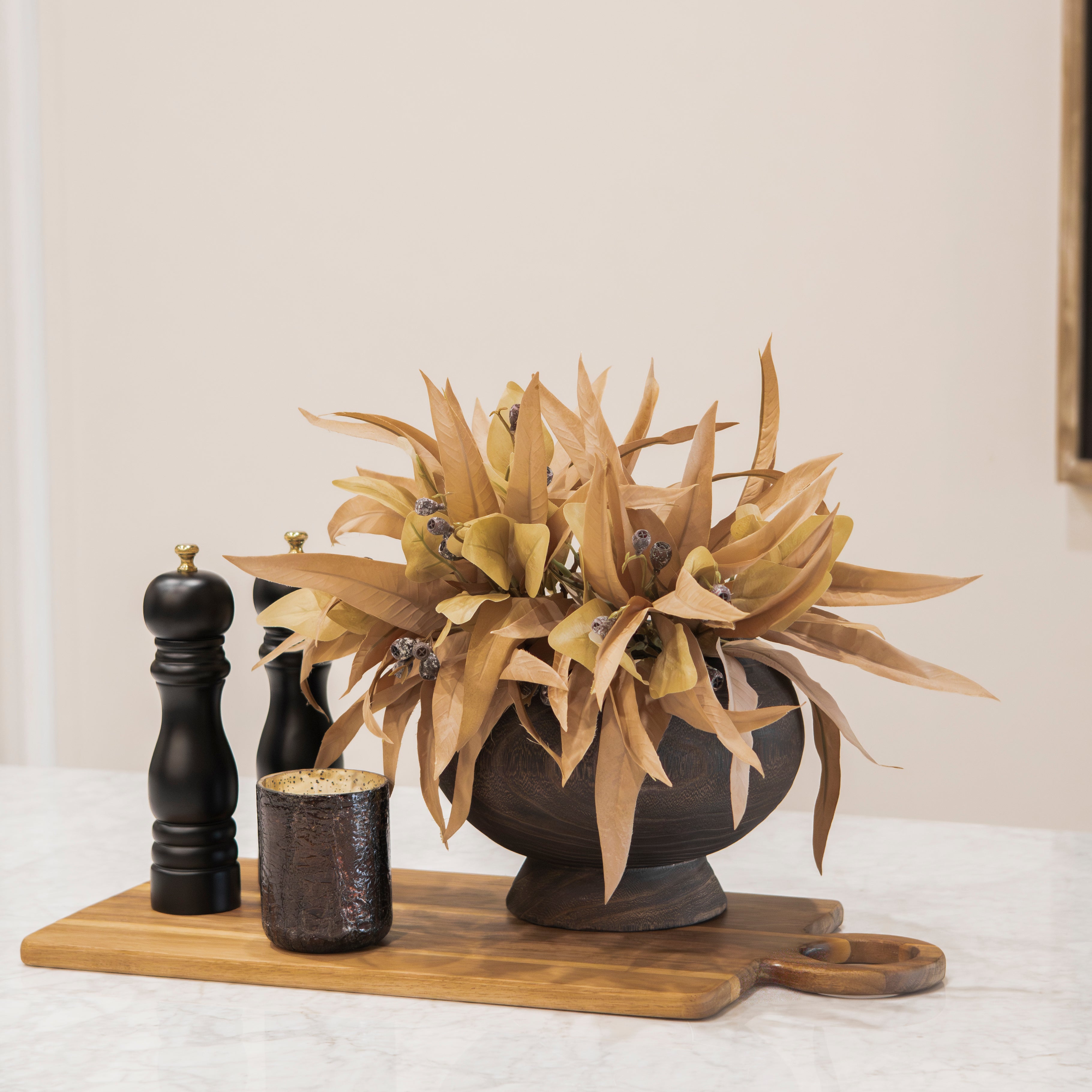 Decorative fall kitchen bundle with a plant, candles, and a cutting board on a white surface.