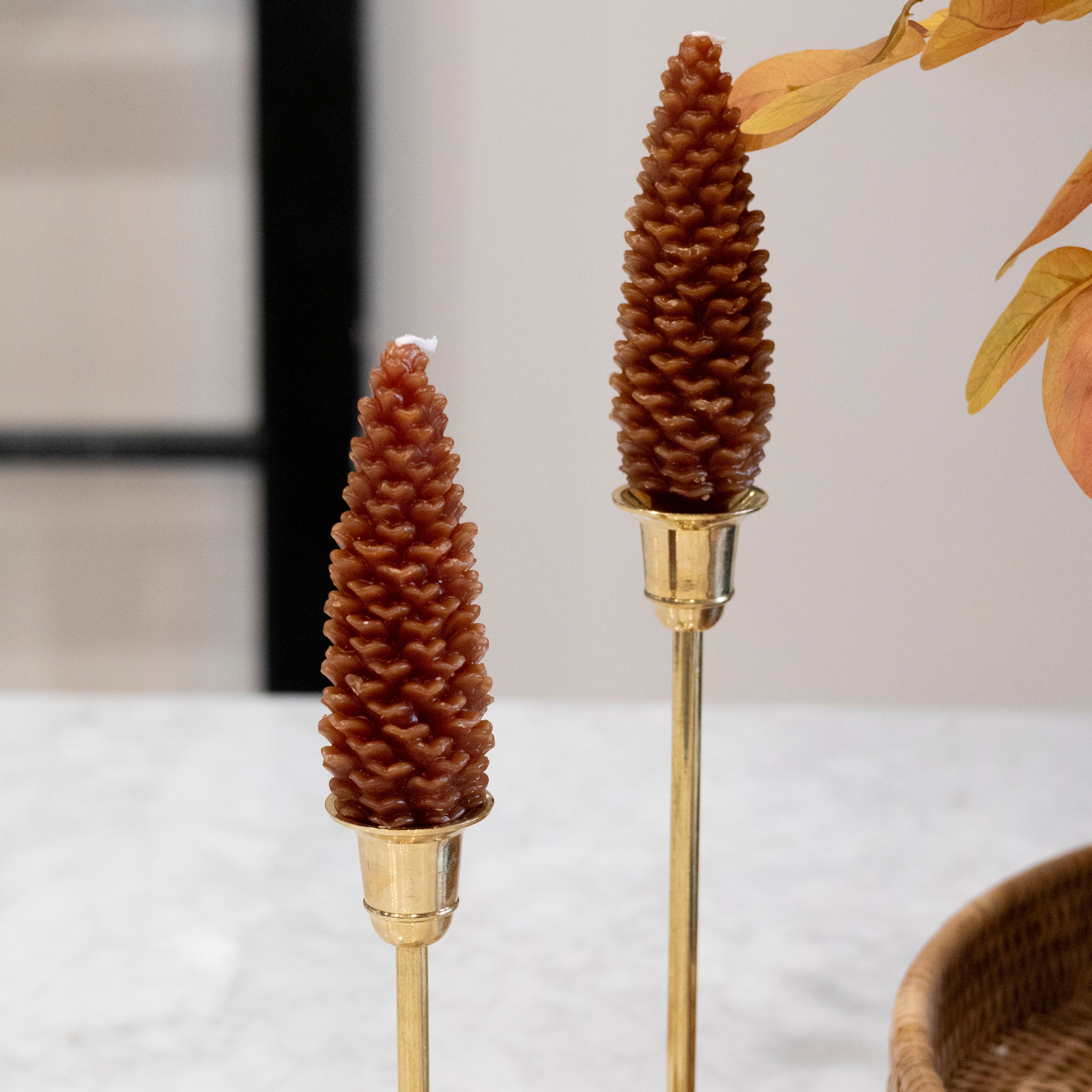 Two decorative candles shaped like pine cones on gold stands with a blurred background.