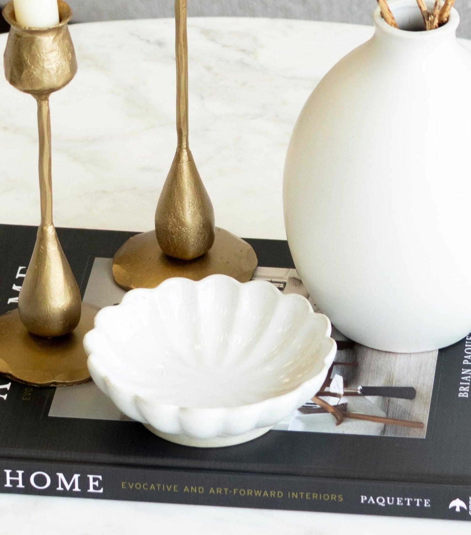 Decorative setup on a coffee table with a white vase, gold candle holders, and a book titled &