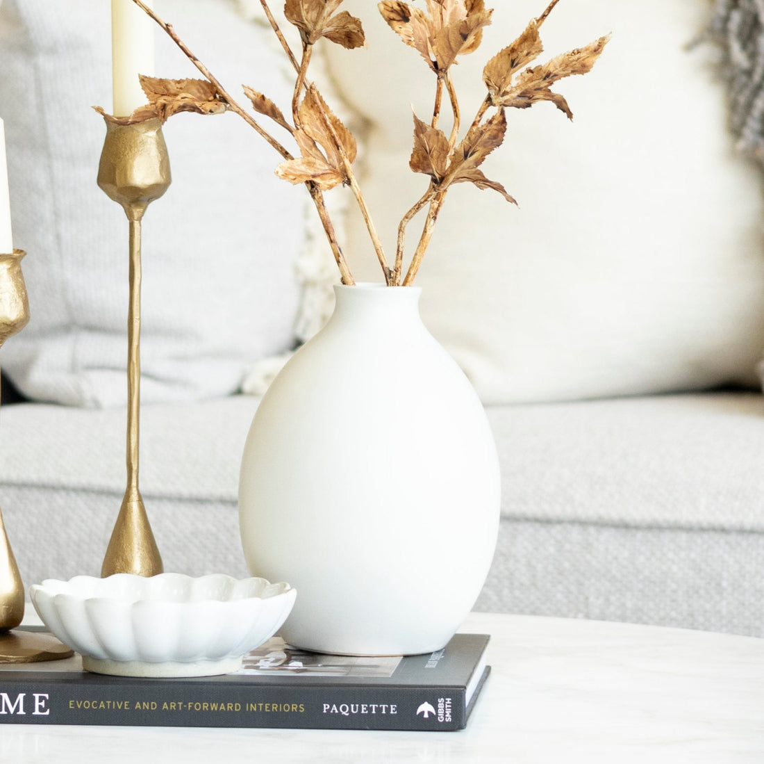Living room with a white sofa, decorative vase, and candles on a coffee table.