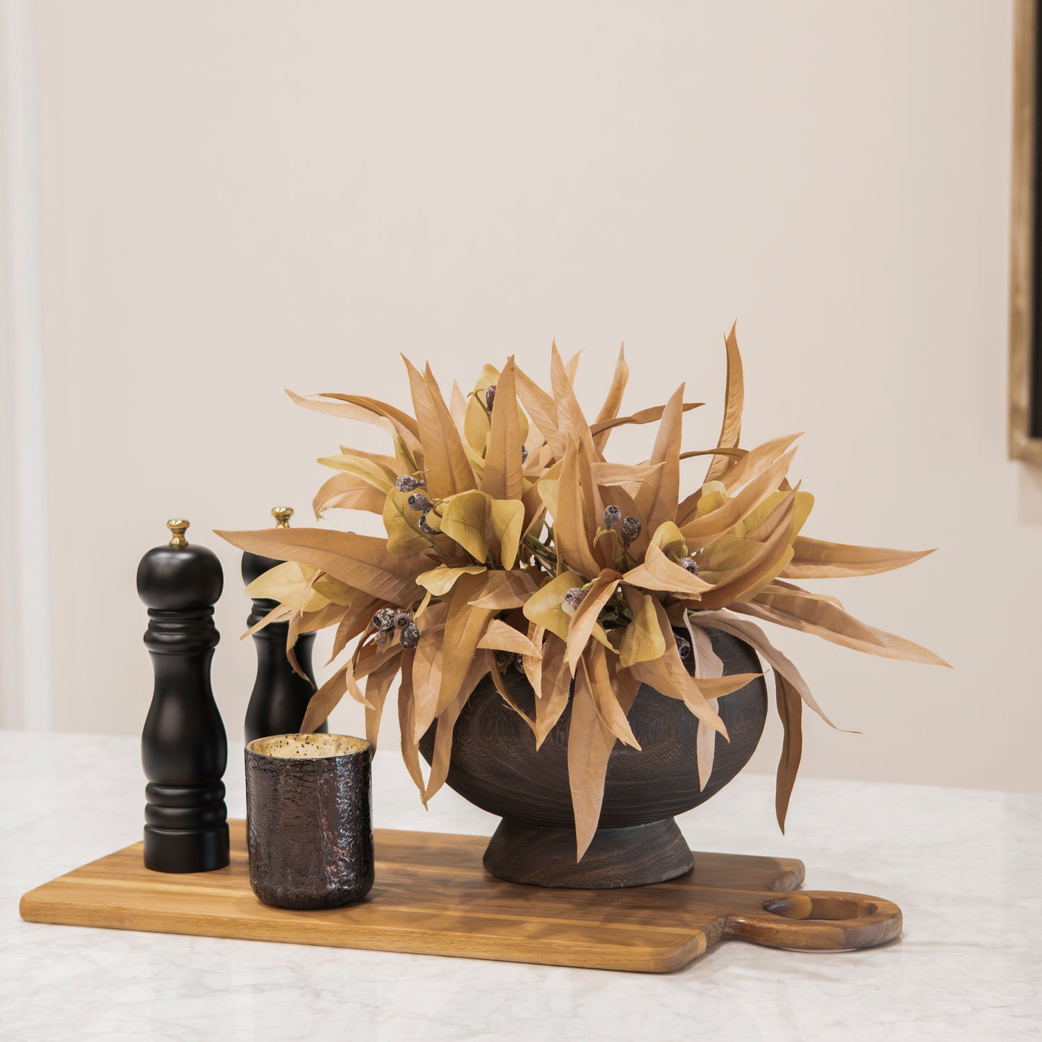 Decorative fall kitchen bundle with a plant, candles, and a cutting board on a white surface.
