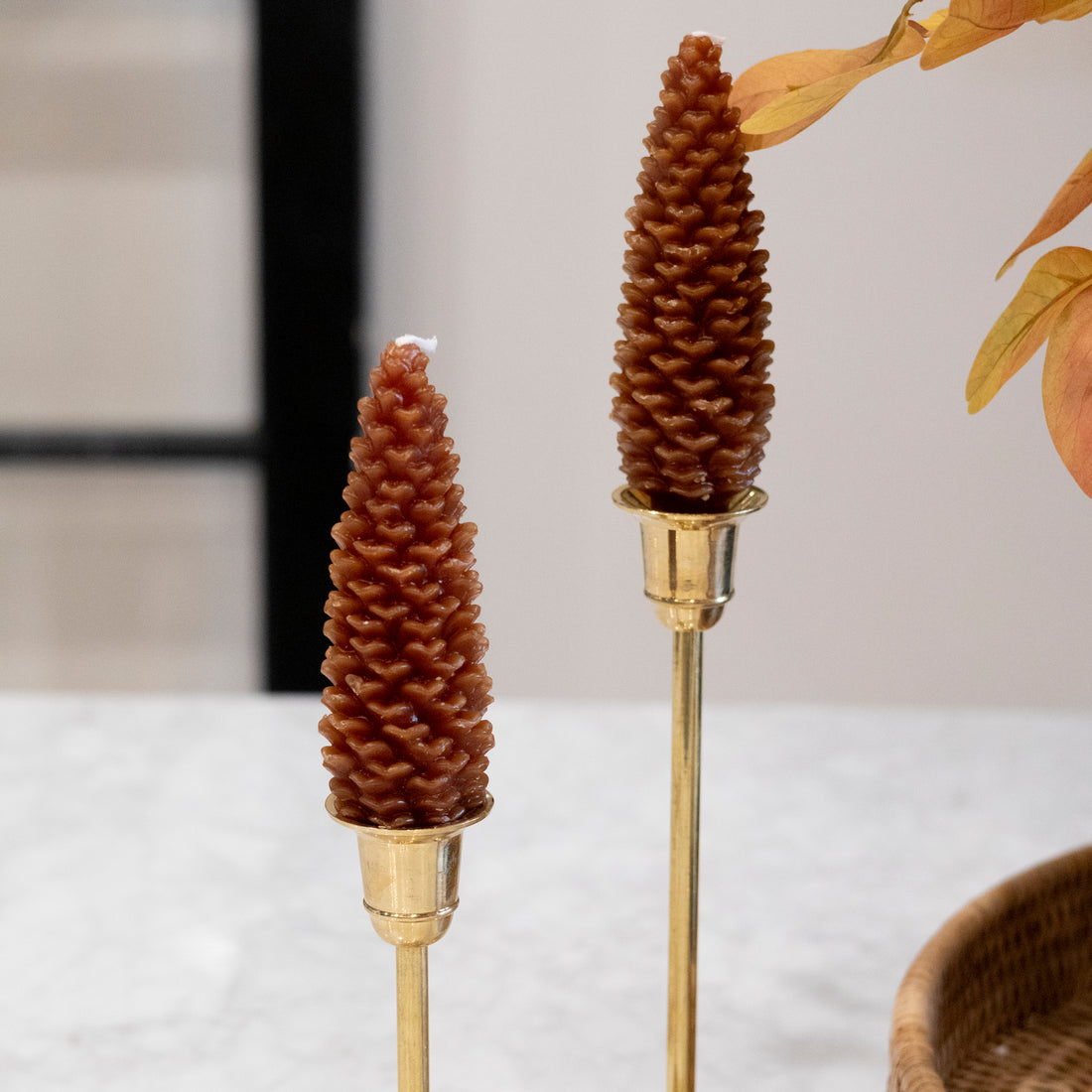 Two decorative candles shaped like pine cones on gold stands with a blurred background.