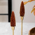 Two decorative candles shaped like pine cones on gold stands with a blurred background.